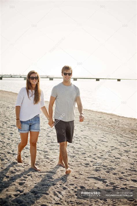 Couple holding hands while walking on shore — young, Beach Holiday - Stock Photo | #151402126