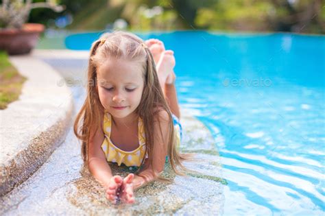 Closeup of Cute little girl in the swimming pool looks at camera Stock Photo by travnikovstudio