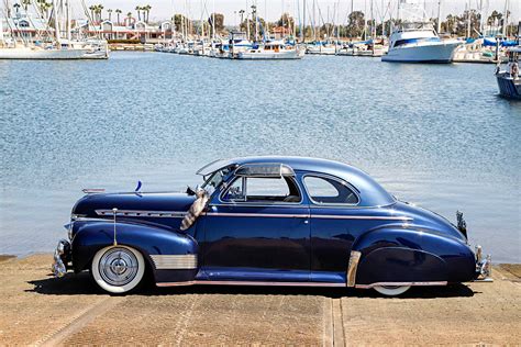 an old blue car parked on the side of a road next to a body of water