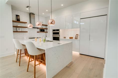 Modern white kitchen with wood accents, floating shelves, quartz waterfall island and copper ...