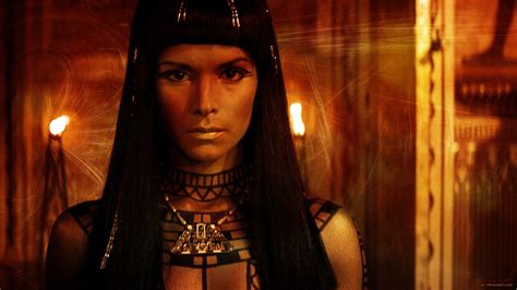 a woman with long black hair and an egyptian headdress is standing in front of candles