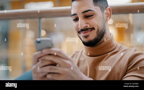 Close-up young arab guy holding phone looking at screen smartphone smiling receive nice email ...