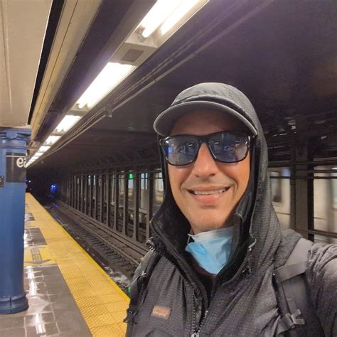 a man wearing sunglasses and a hat stands in front of a subway train at the station