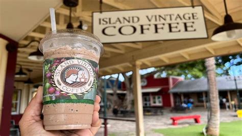 a person holding up a drink in front of a sign that reads island vintage coffee