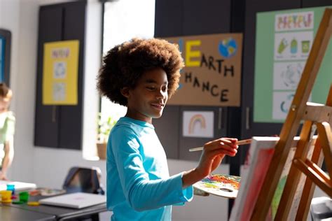 Premium Photo | Happy african american schoolboy painting using brush and easel in school art class