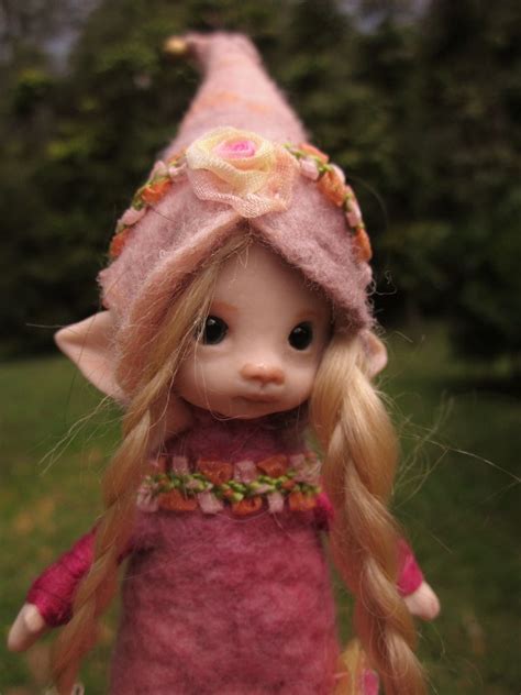 a doll with long blonde hair wearing a pink hat and dress, standing in the grass