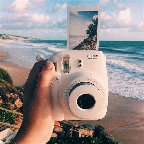 someone holding up a polaroid camera to take a photo on the beach with waves in the background