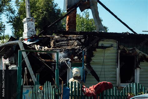 a firefighter pours water on a burned house. the wreckage of a wooden building destroyed by fire ...