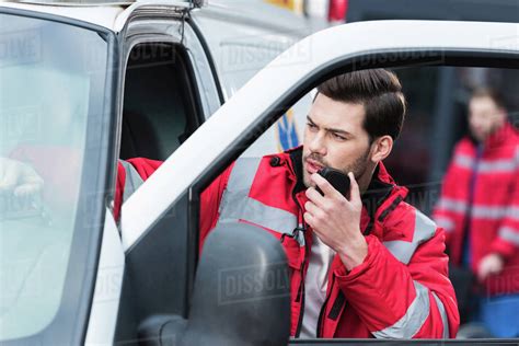 Young handsome male paramedic standing near ambulance and talking by portable radio - Stock ...