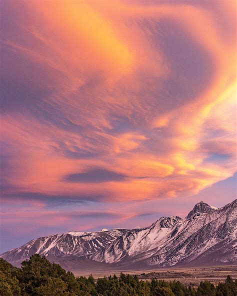 the mountains are covered in snow and clouds as the sun is setting over them,