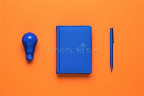 A Blue Light Bulb, a Blue Notebook and a Blue Pen on an Orange ...