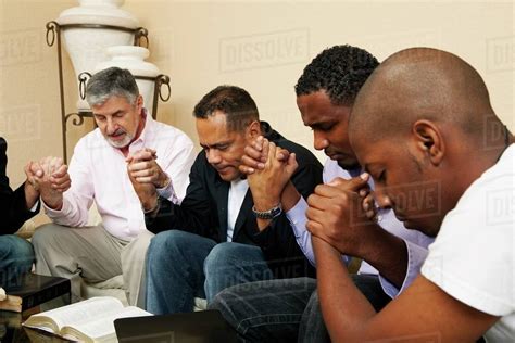 A Group Of Men Praying Together With An Open Bible - Stock Photo - Dissolve