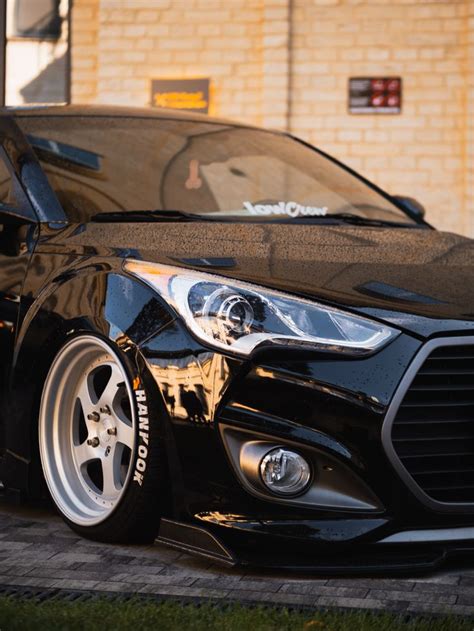 the front end of a black car parked in front of a brick building with grass