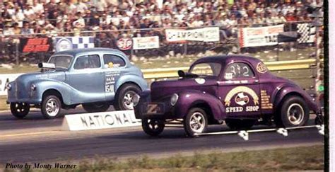 two old cars racing on a track in front of an audience