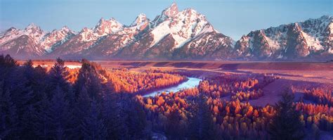 the mountains are covered in snow and orange trees, with a river running between them