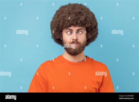 Portrait of crazy funny man with Afro hairstyle wearing orange T-shirt standing with crossed ...