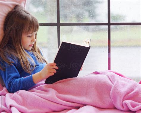 "A Young Girl Sits In A Window Seat Reading A Book On A Rainy Day." by Stocksy Contributor "Tana ...