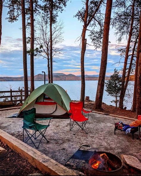 there is a tent set up in the woods by the water with chairs around it