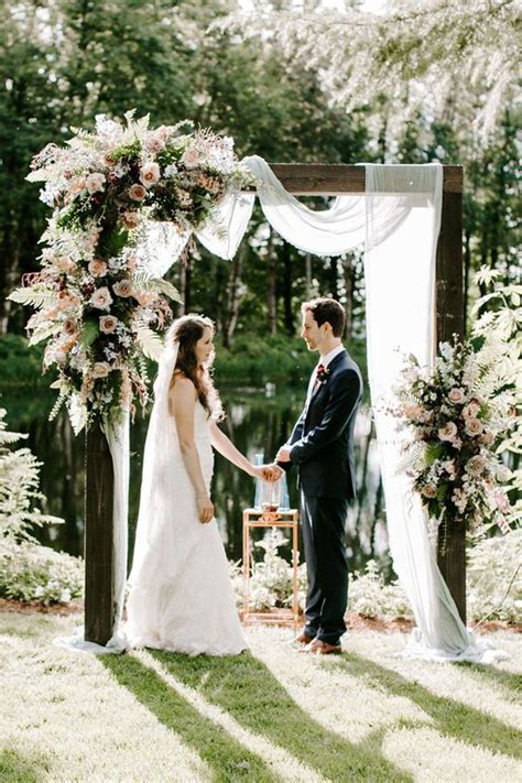 a bride and groom standing in front of an outdoor ceremony arch with ...