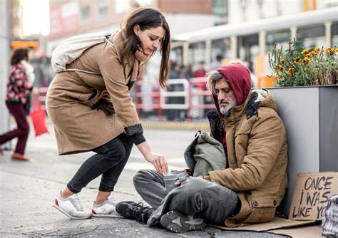 Young Woman Giving Money To Homeless Beggar Man Sitting in City. Stock ...