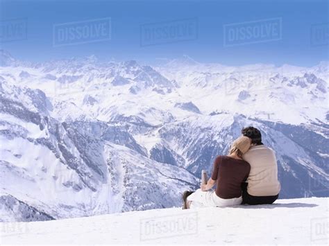 Couple sitting in the snow hugging - Stock Photo - Dissolve