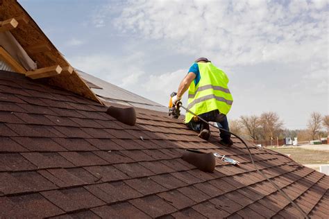 Construction worker putting the asphalt roofing (shingles) with nail ...