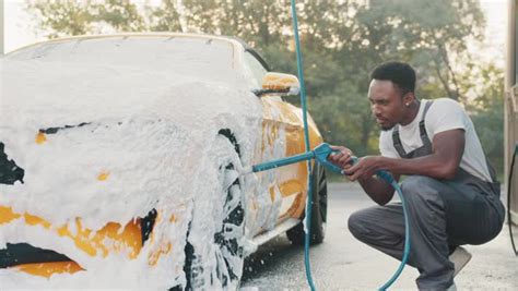 Car wash outdoors concept. Luxury modern car in foam. Young African man ...