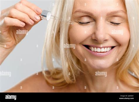 Close-up portrait of magnificent middle-aged blonde woman using skin care product, charming lady ...