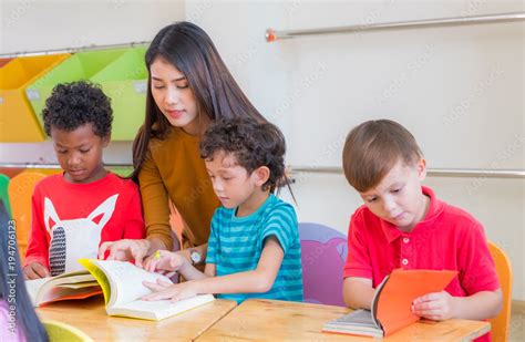 Asian female teacher teaching diversity kids reading book in classroom ...