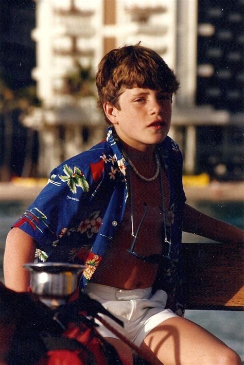 a young man sitting on top of a wooden bench next to a body of water