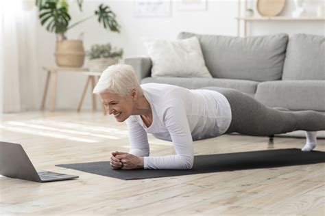 Sporty senior woman doing yoga plank while watching tutorial on laptop - Rejuvage