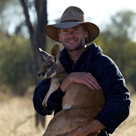 a man holding a kangaroo in his arms and wearing a hat on top of it