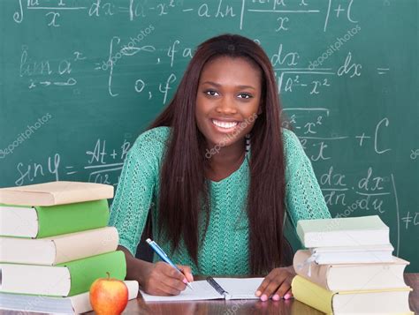 Confident female teacher writing in book at classroom desk Stock Photo ...