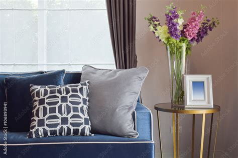 Navy blue modern classic sofa and retro, gray and blue pillows with a lovely orchid vase on side ...