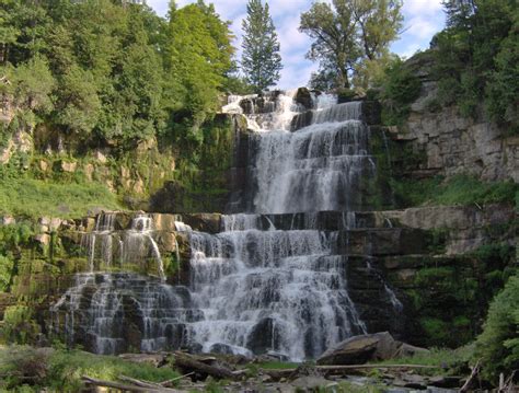 a large waterfall with lots of water cascading down it's sides, surrounded by lush green trees