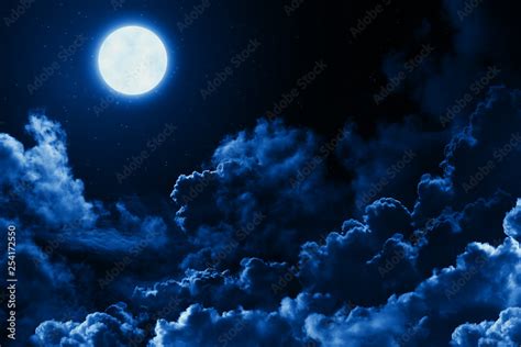 Mystical bright full moon in the midnight sky with stars surrounded by dramatic clouds. Dark ...