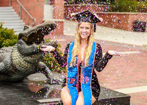 a woman in a graduation cap and gown sitting on a bench with a large alligator