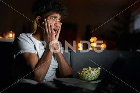 Young guy looking terrified while watching horror movie alone using ...