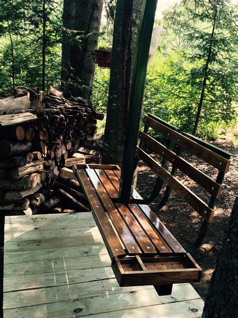 a wooden bench sitting next to a pile of logs in the woods on a sunny day