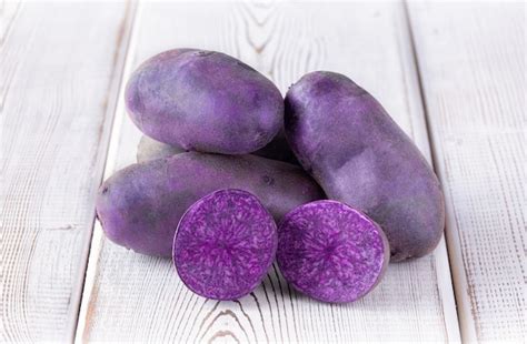 Premium Photo | Rare purple potatoes with two cut halves on white wooden table