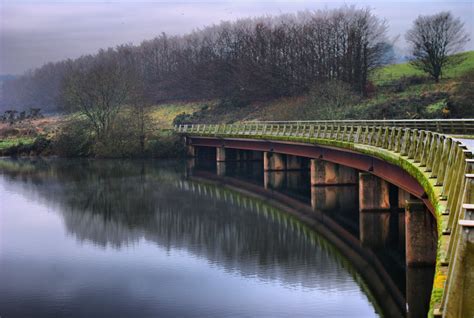 a bridge that is over some water with trees on the side and hills in the background