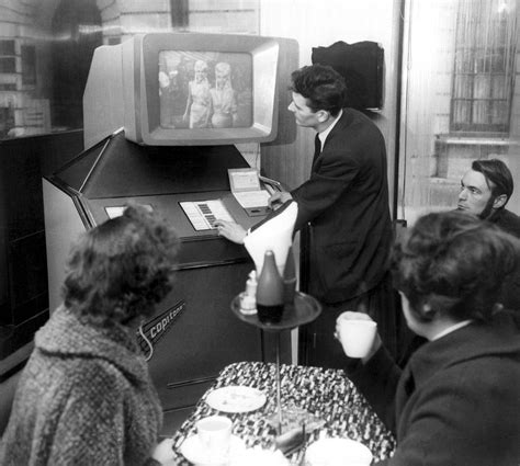 People gathered around a Scopitone video jukebox, watching a precursor to the music video. Paris ...