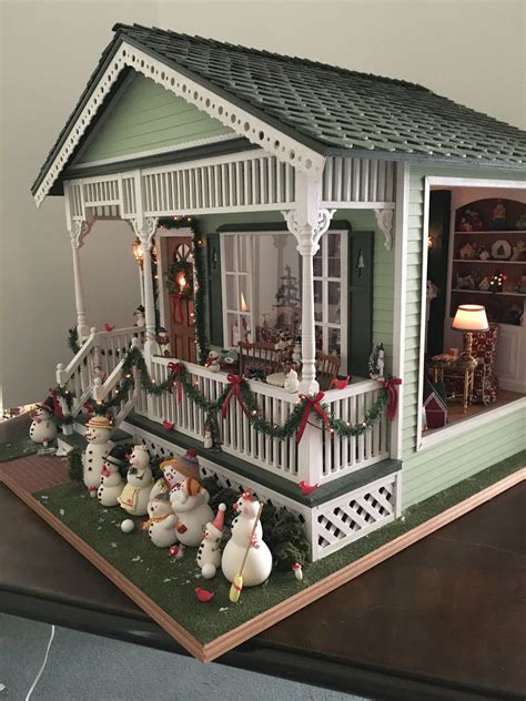 a doll house with snowmen and christmas decorations on the front porch, including lights