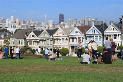 a group of people sitting on top of a lush green field next to tall buildings