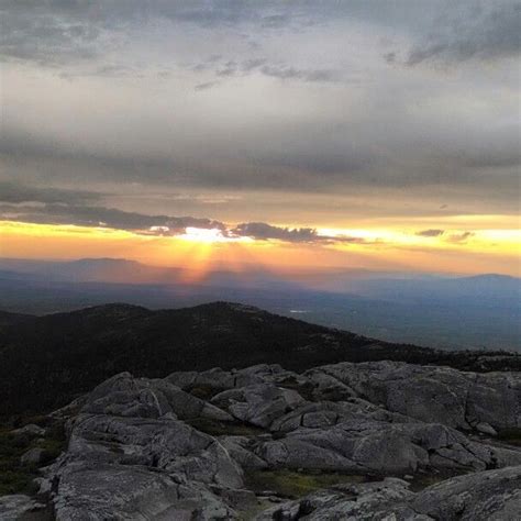 the sun is setting over some rocks on top of a mountain with mountains ...