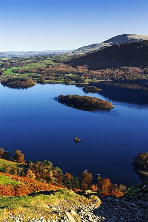 a large body of water surrounded by hills and trees in the distance with blue sky