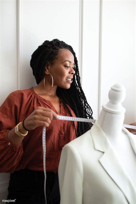 Black fashion designer measuring a white coat on a pinnable mannequin ...