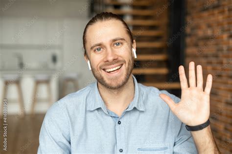 Young European man looking at the camera, smiling and waving the hand ...