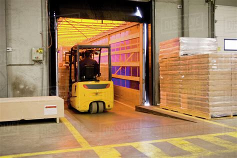 Forklift operator loading wrapped pallets of cardboard boxes onto ...