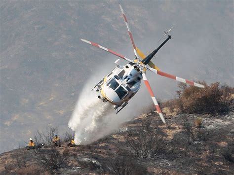 A ground crew watches as a firefighting helicopter drops water on a ...